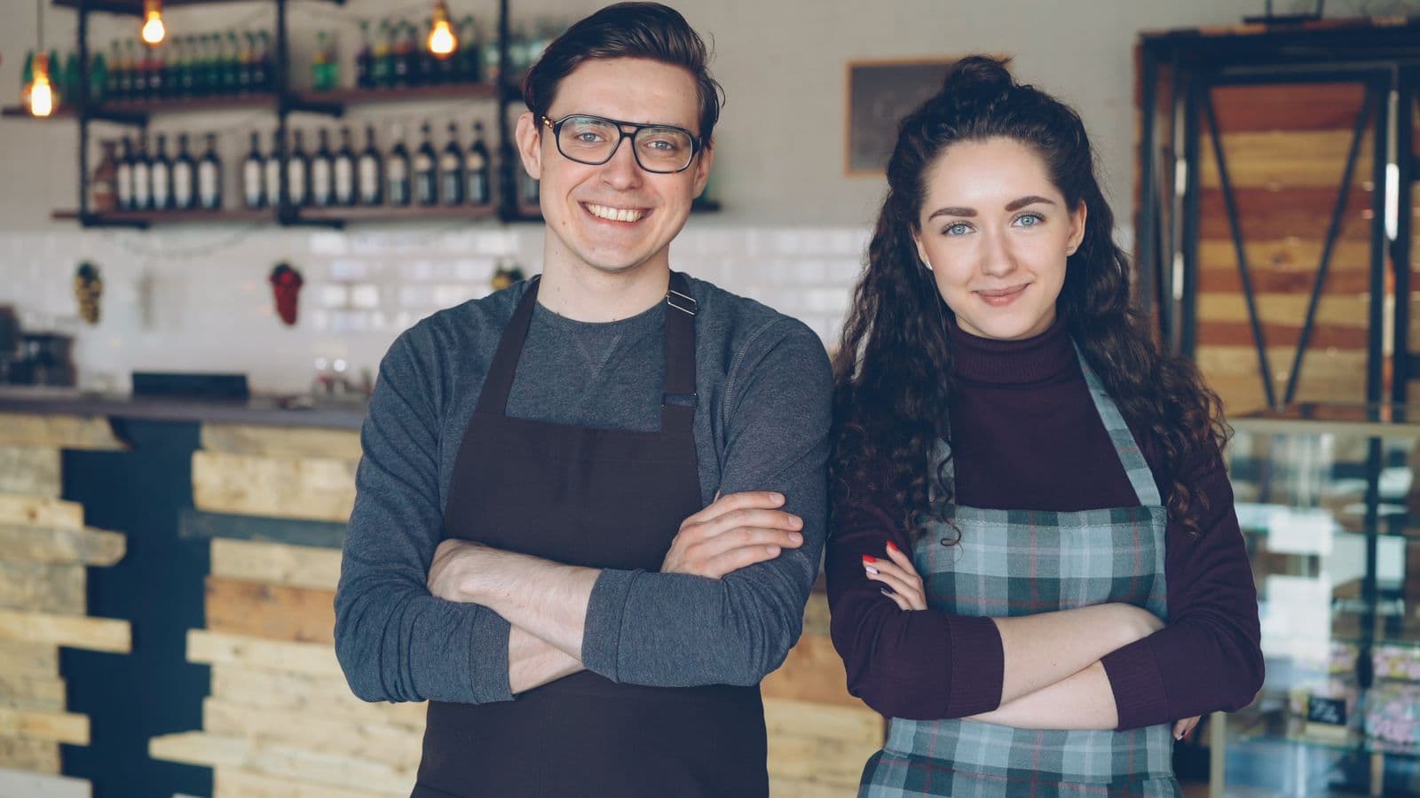 Two café owners in aprons, arms folded, smiling in front of their counter