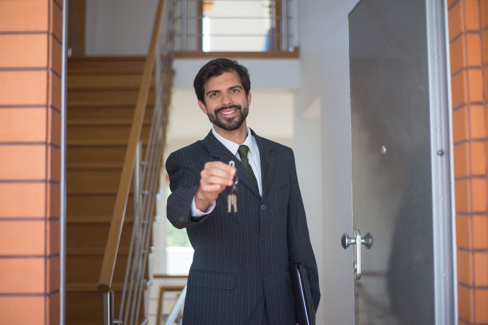 A man in a suit holding out a set of house keys at an open front door