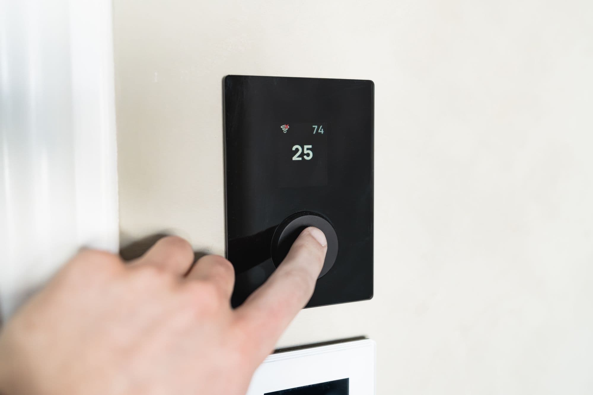A hand pressing the dial of a smart thermostat on a wall at home