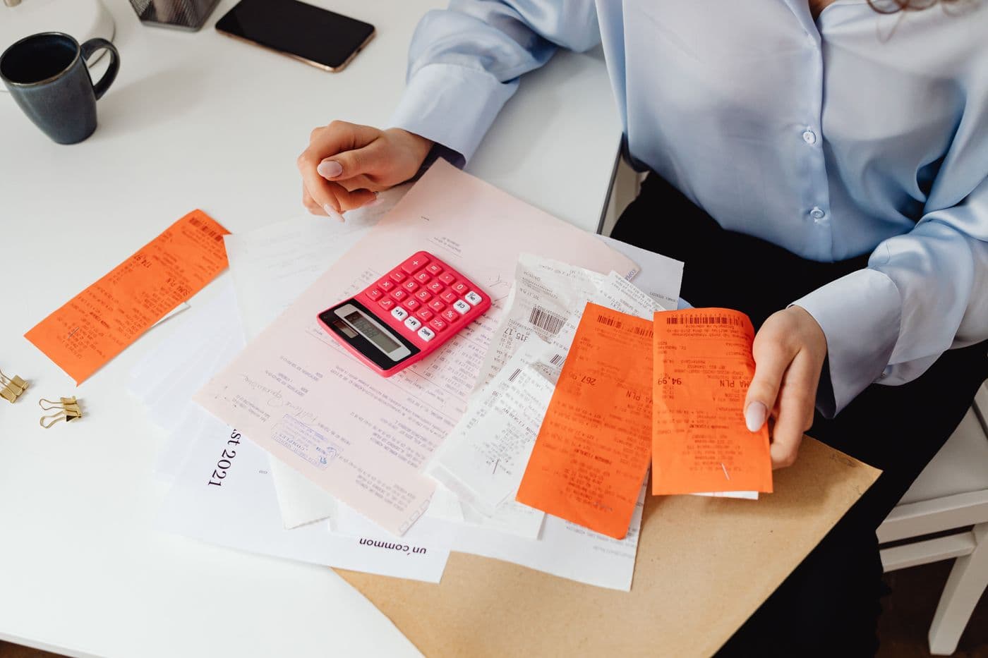 Hands working through a pile of bills and receipts with a pink calculator