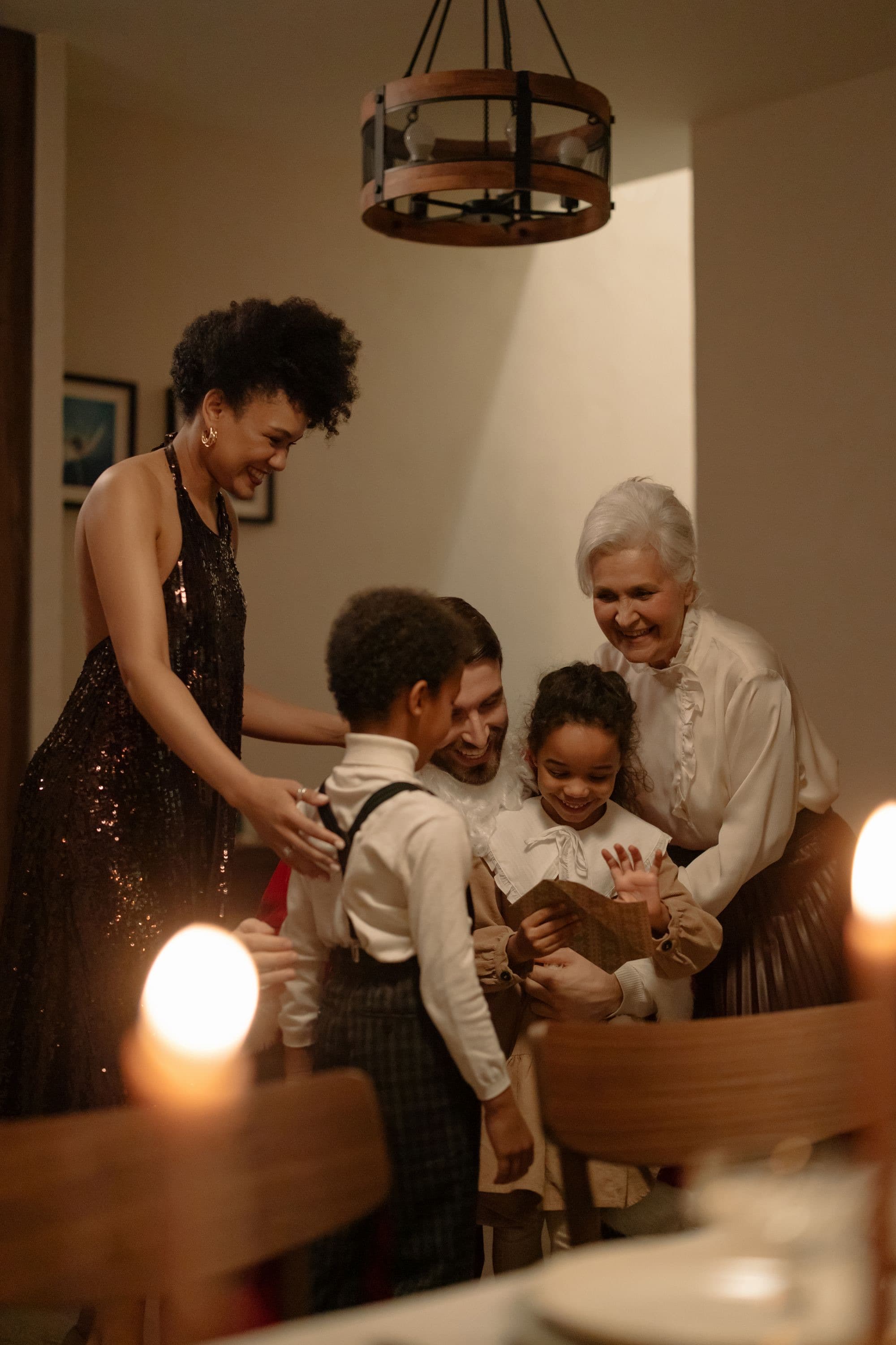 A family of different ages and backgrounds gathered at home, a grandmother and two young children laughing together over a card