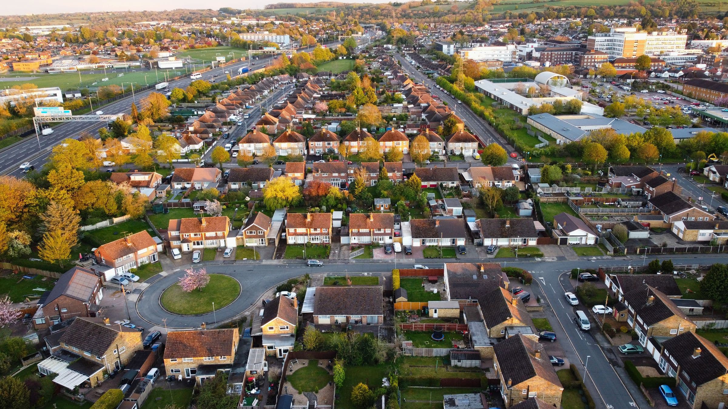 Rows of houses and gardens in an English town from the air, lit by a low evening sun