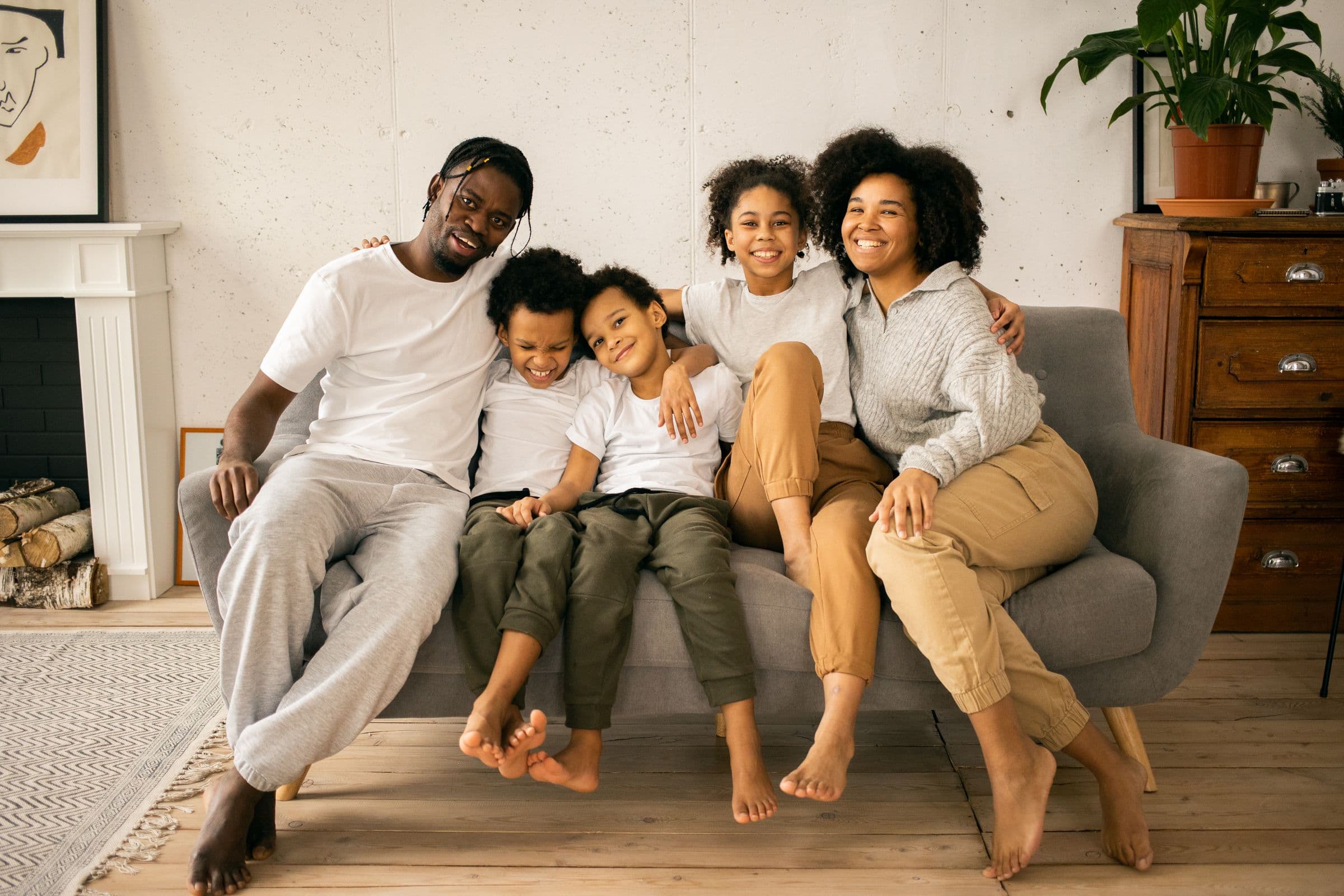 A family of five sitting close together on a sofa at home, smiling