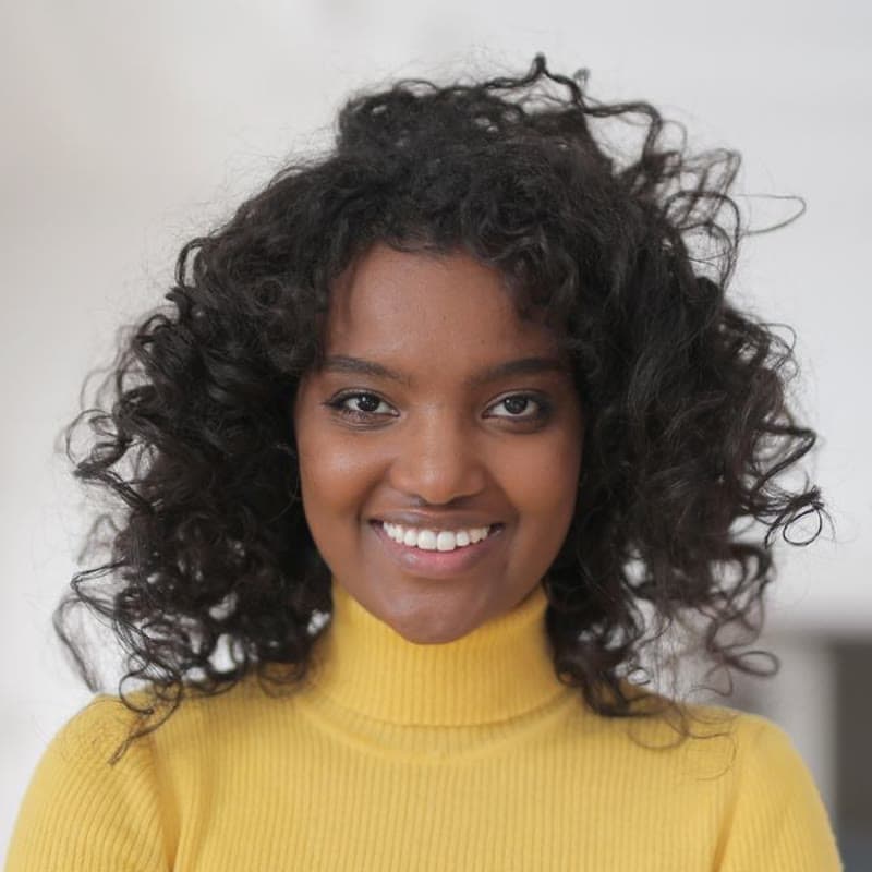 A smiling young woman in a yellow jumper at home