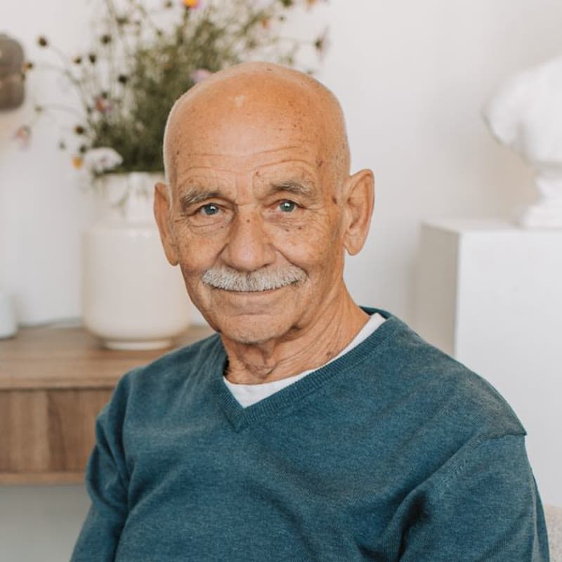 An older man in a blue jumper smiling at home