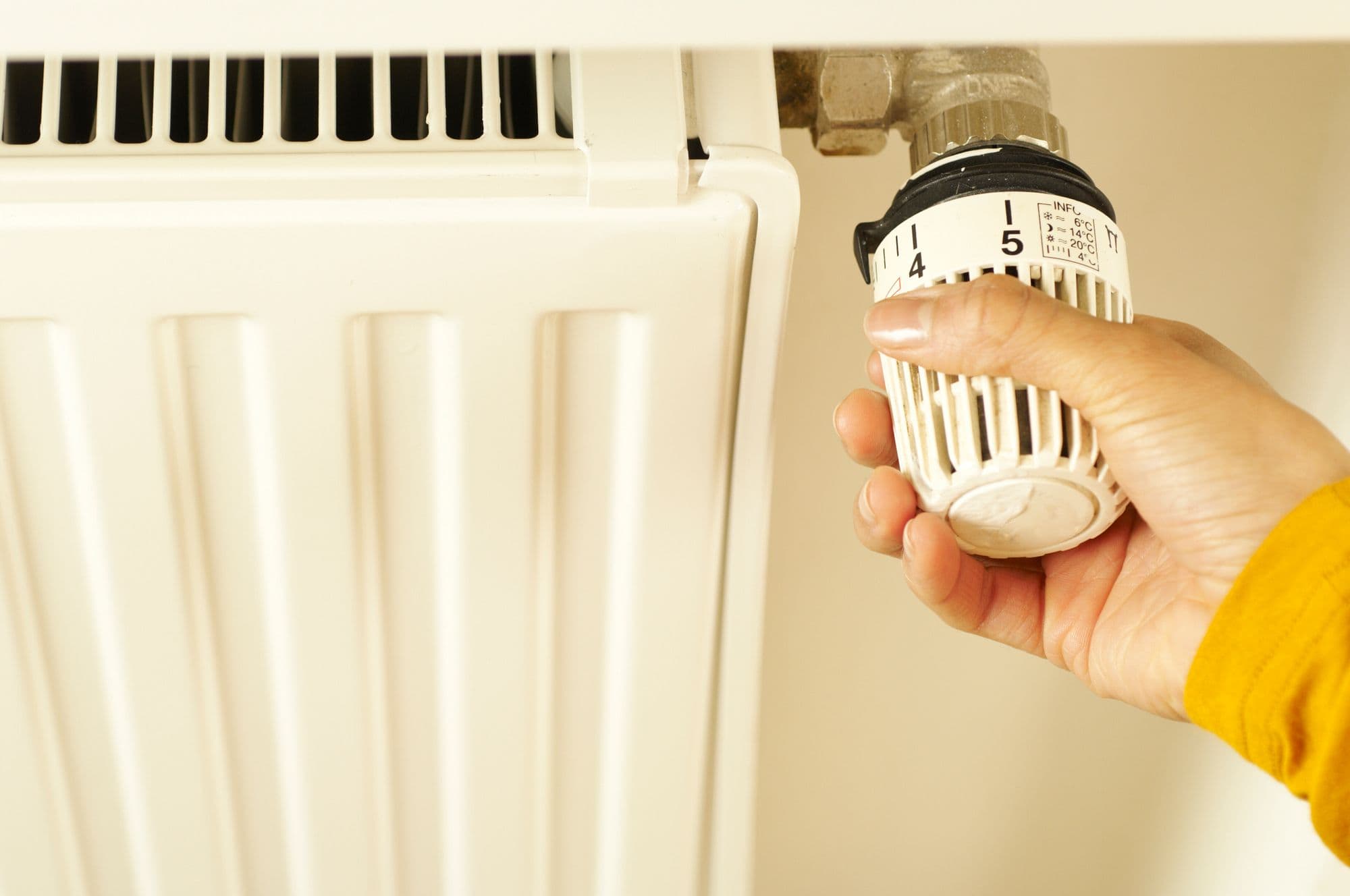 A hand turning the thermostatic valve on a white radiator at home