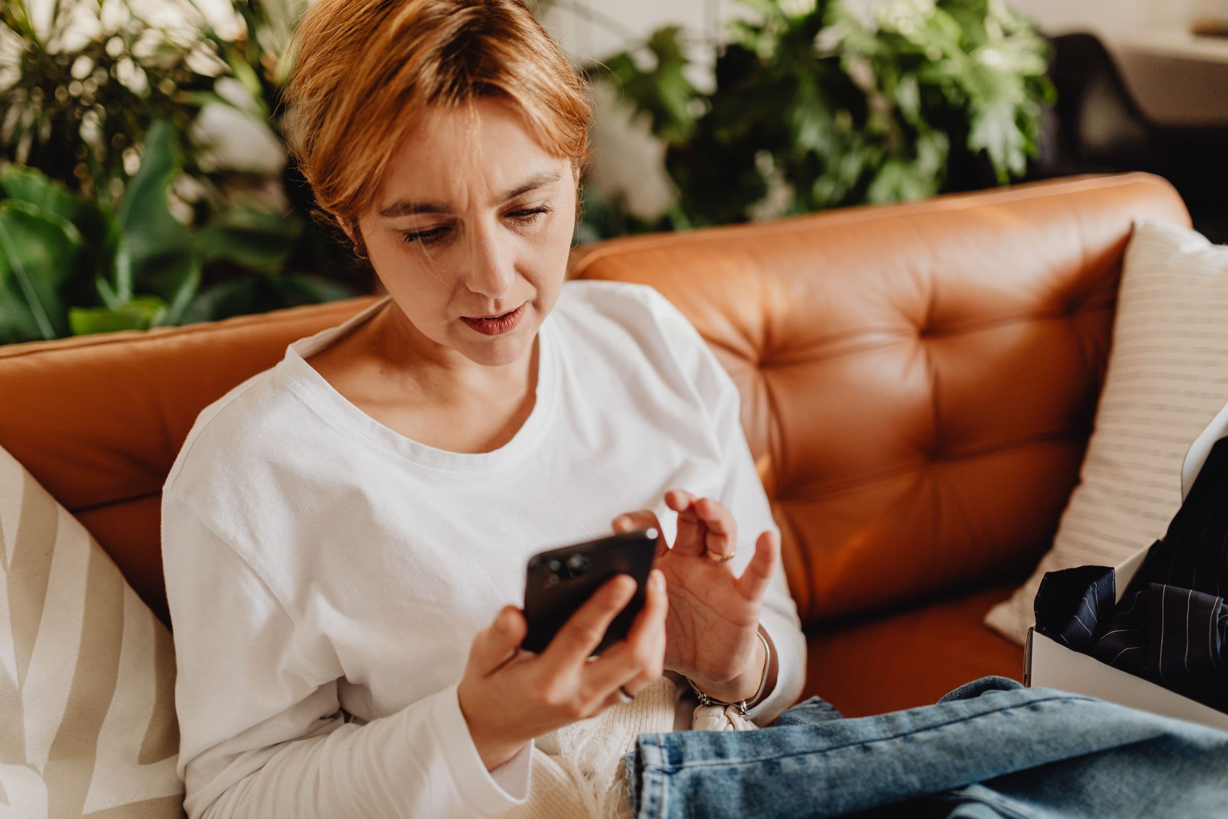 A woman on a leather sofa at home, checking something on her phone
