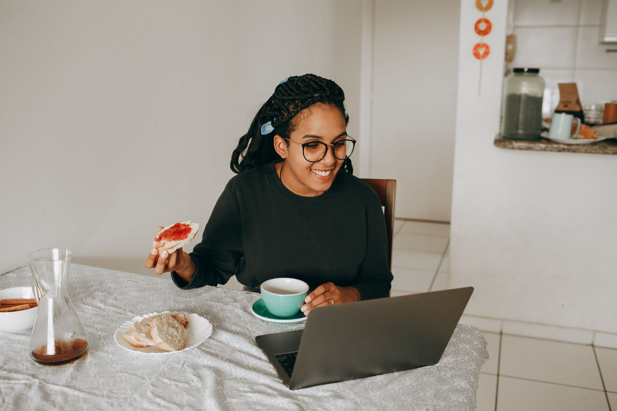 A woman smiling at her laptop over breakfast at her kitchen table
